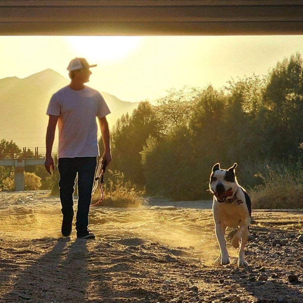 Roman walking his dog on a desert trail at sunset